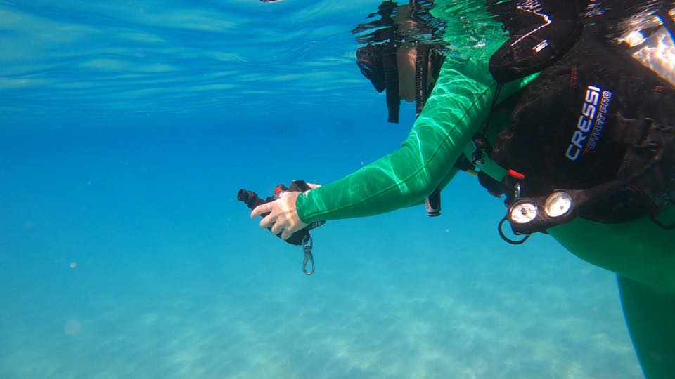 A diver with an underwater camera and lights over white sand