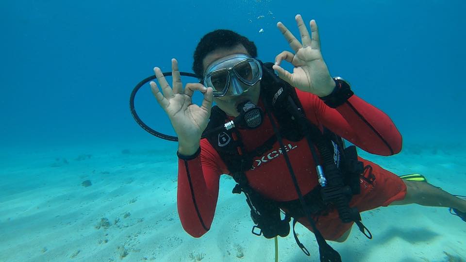 A diver in a red rash guard giving two OK signs