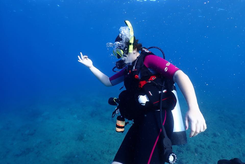 A student hovering in blue water, giving the OK sign