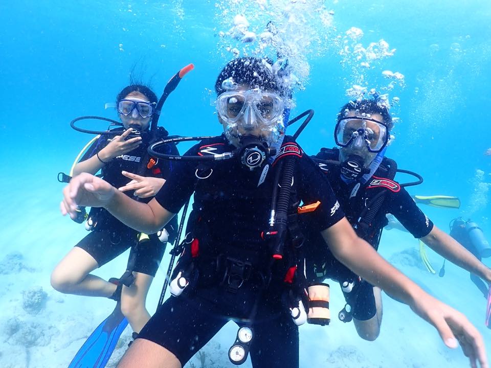 Three young divers giving signals and smiling in clear blue water