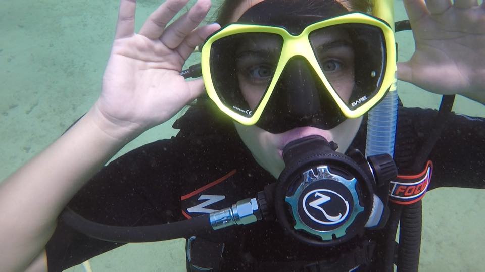 A first-time diver waving at the camera underwater, mask on