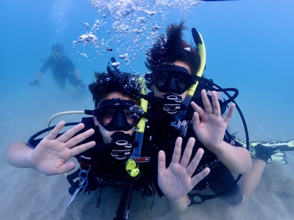 Two young students waving underwater during a PR Dive course