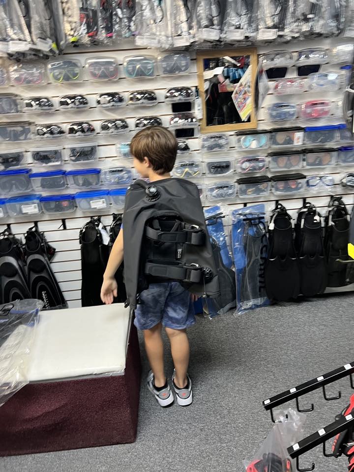 A young diver being fitted for a BCD in the shop, in front of the mask wall