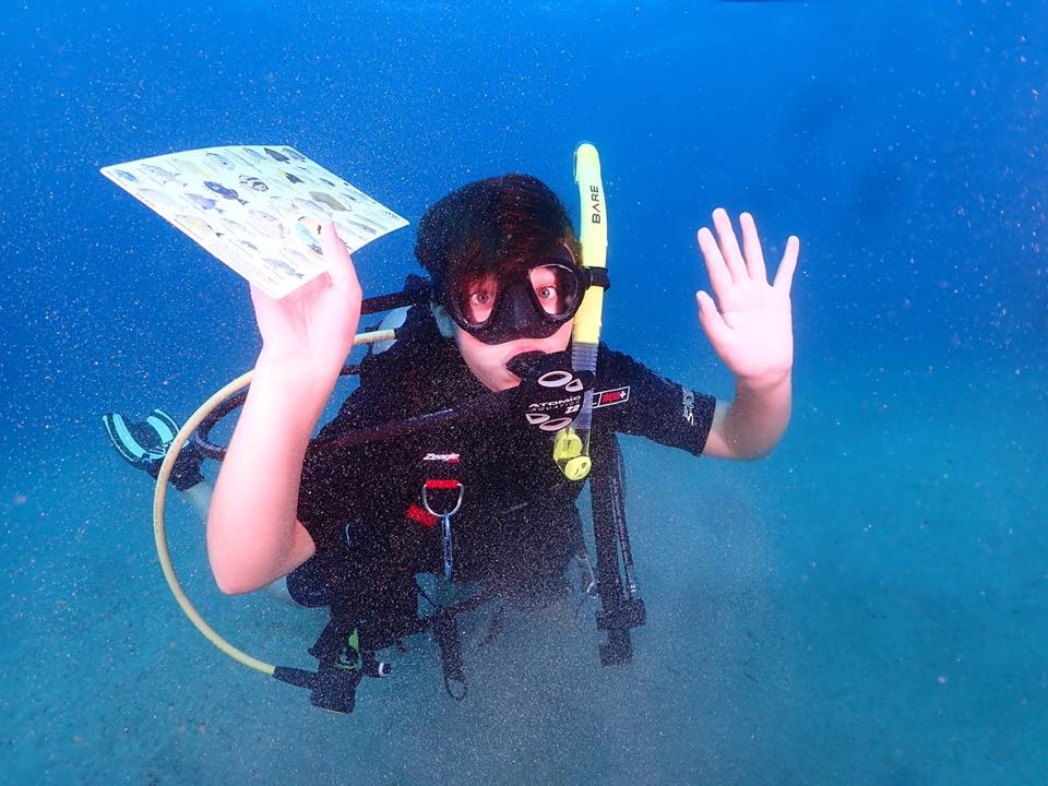 A young student waving and holding a fish ID card